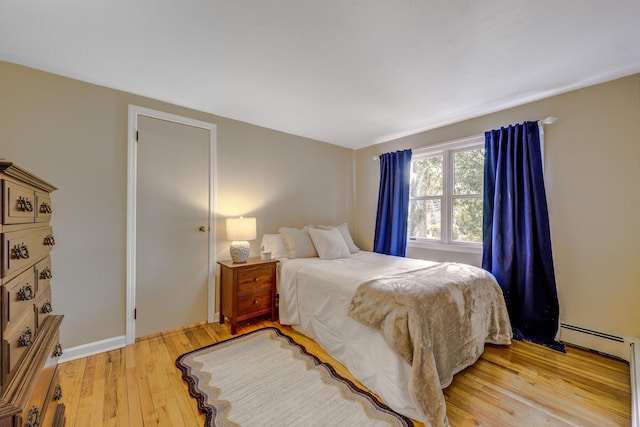 bedroom with a baseboard heating unit and light wood-style floors