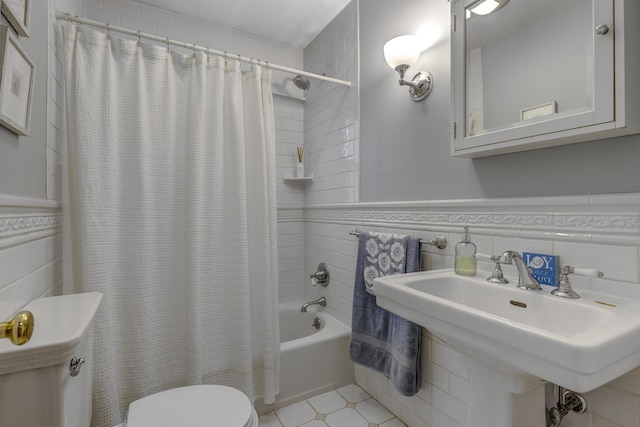 full bathroom with a wainscoted wall, shower / bathtub combination with curtain, toilet, a sink, and tile walls