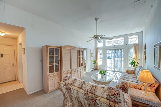 living area with a ceiling fan, a high ceiling, light carpet, and baseboards