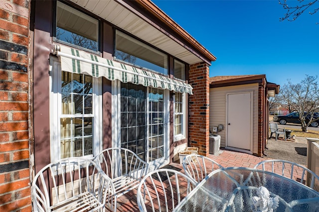 view of exterior entry with brick siding, outdoor dining area, a patio area, and cooling unit