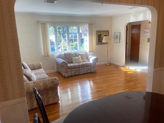 living room with arched walkways, wood finished floors, visible vents, baseboards, and ornamental molding