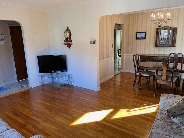 living room featuring arched walkways, baseboards, an inviting chandelier, and wood finished floors