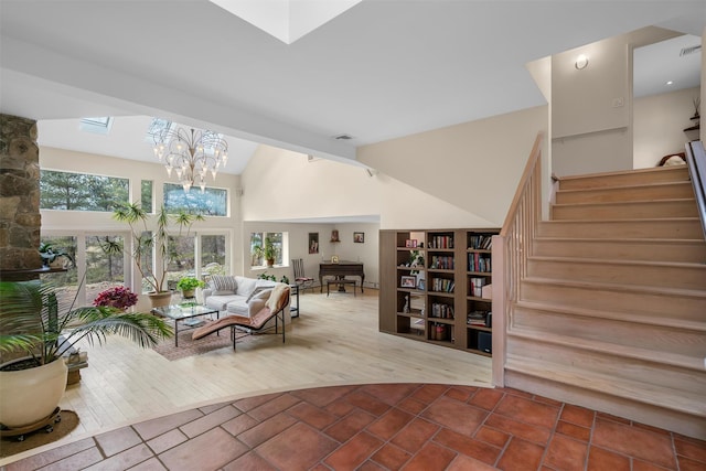 living area with visible vents, lofted ceiling with skylight, a chandelier, stairs, and wood finished floors