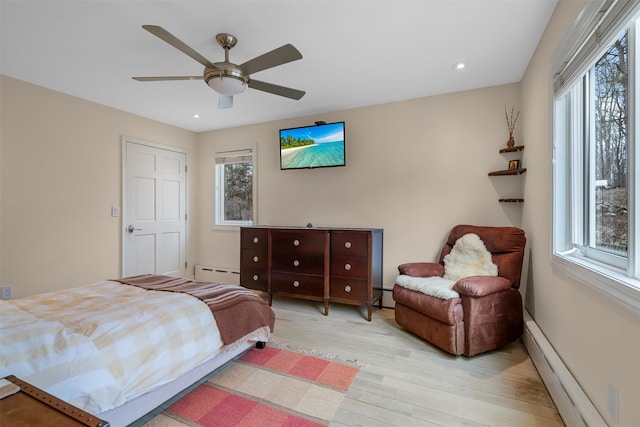 bedroom with a baseboard radiator, multiple windows, and light wood-style flooring