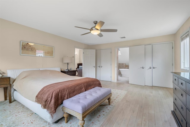 bedroom featuring visible vents, two closets, light wood-style flooring, ensuite bathroom, and a ceiling fan