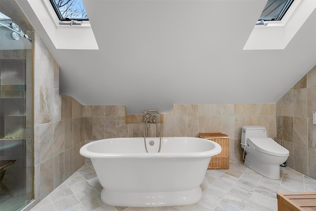 full bathroom featuring a freestanding tub, lofted ceiling with skylight, toilet, and tile walls