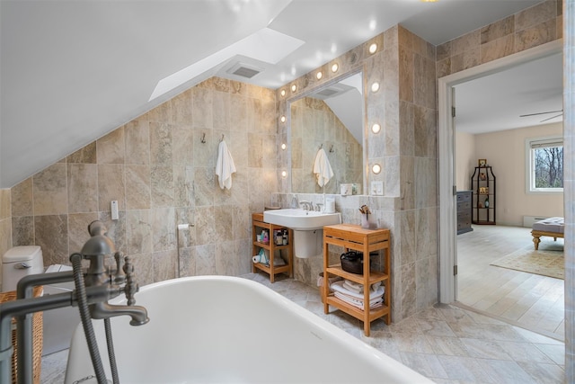 bathroom with visible vents, tile walls, lofted ceiling, and a freestanding tub