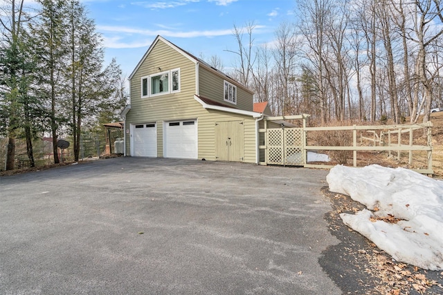 view of property exterior featuring driveway, an attached garage, and fence