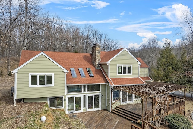 rear view of property featuring a shingled roof, a chimney, and a wooden deck