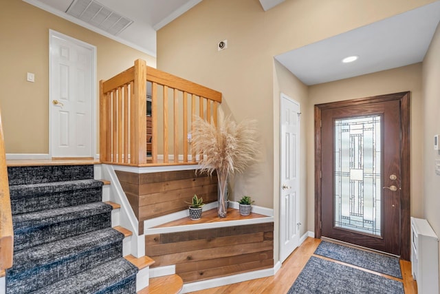 entryway with radiator, wood finished floors, visible vents, stairs, and crown molding