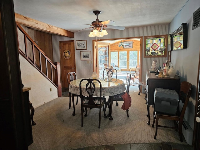 dining area featuring carpet, wallpapered walls, ceiling fan, and stairs