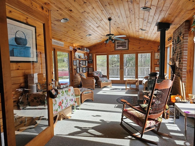 sitting room with wooden walls, lofted ceiling, wooden ceiling, a wood stove, and carpet flooring