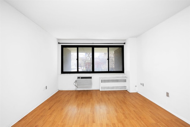 empty room with radiator, a wall mounted AC, light wood-style flooring, and baseboards