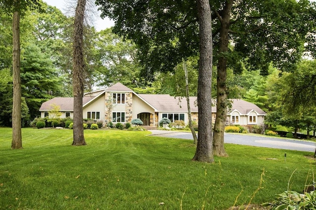 view of front facade featuring aphalt driveway, stone siding, and a front yard