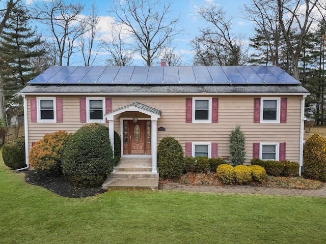 raised ranch with roof mounted solar panels and a front lawn