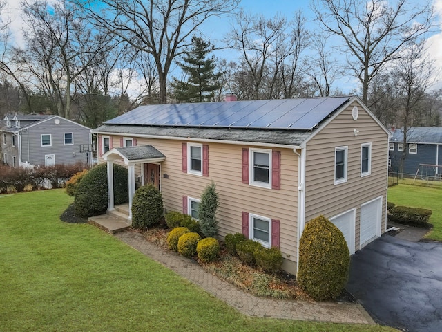 view of side of home with a garage, roof mounted solar panels, a yard, and a chimney