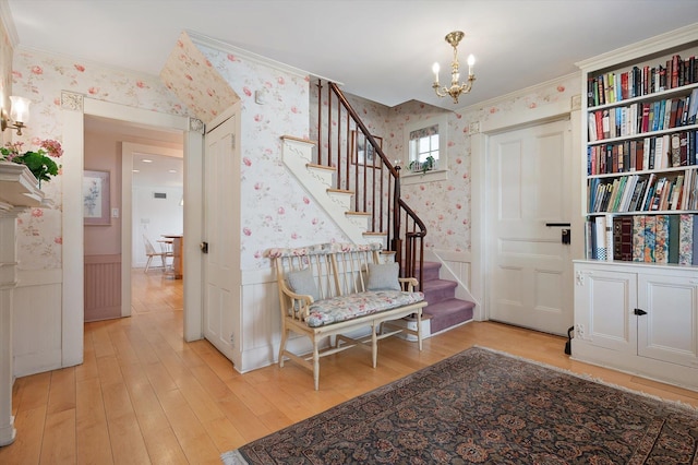 foyer entrance featuring wood finished floors, stairway, wainscoting, wallpapered walls, and an inviting chandelier