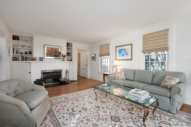 living room with baseboards, a fireplace with flush hearth, wood finished floors, crown molding, and built in shelves