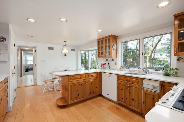 kitchen featuring a peninsula, light wood-style floors, white dishwasher, and a sink