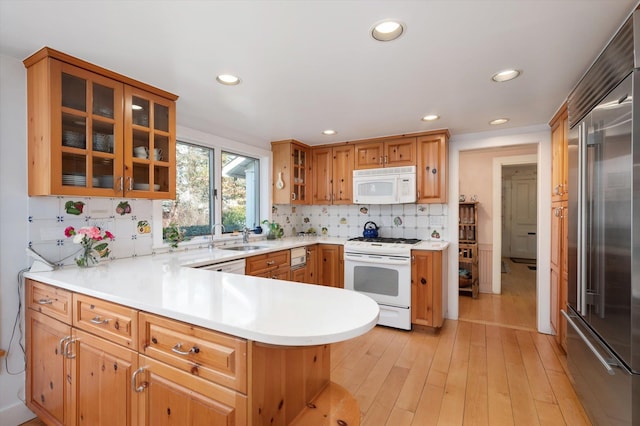 kitchen featuring white appliances, a peninsula, a sink, light countertops, and backsplash