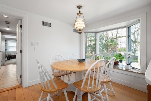 dining area with light wood-type flooring, visible vents, and baseboards