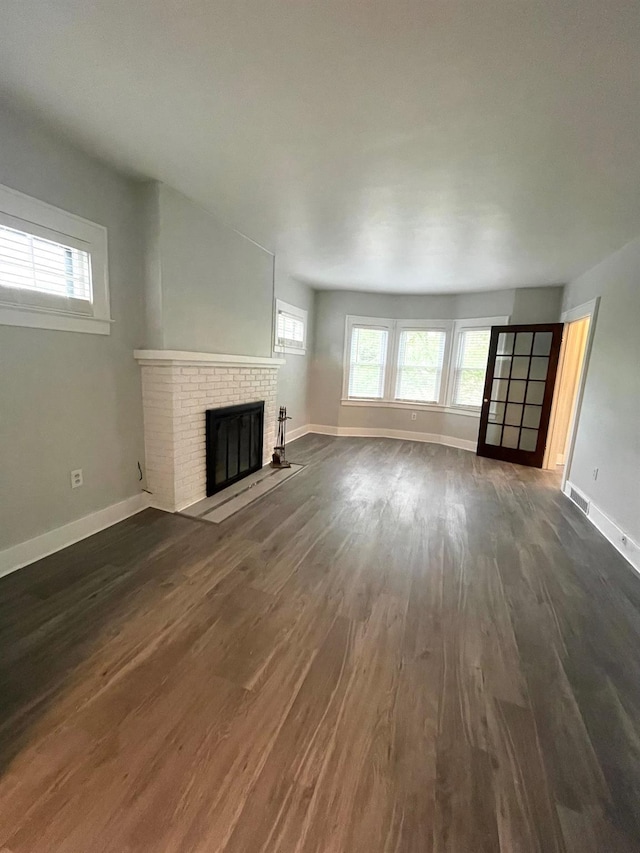 unfurnished living room with a brick fireplace, visible vents, a wealth of natural light, and dark wood-style flooring