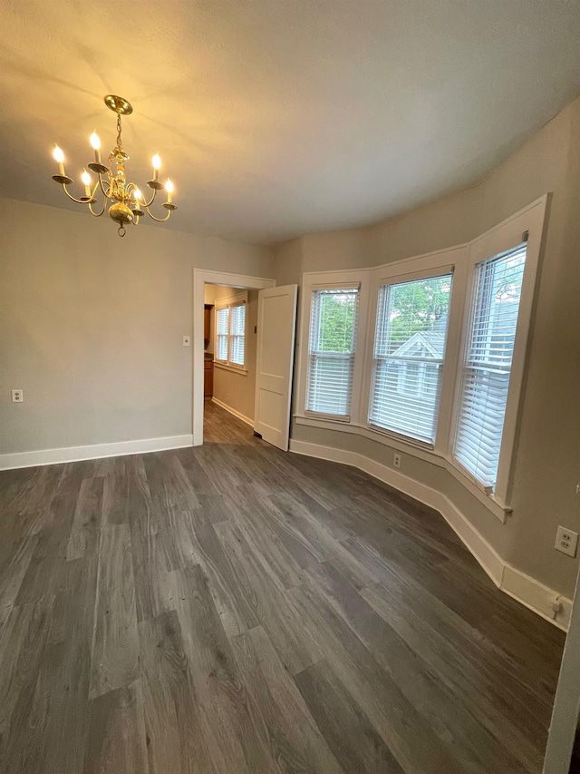 unfurnished living room featuring baseboards, dark wood finished floors, and an inviting chandelier