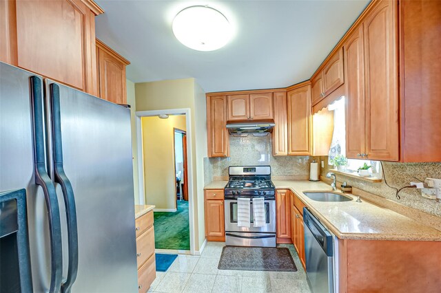 kitchen with backsplash, appliances with stainless steel finishes, a sink, light stone countertops, and under cabinet range hood