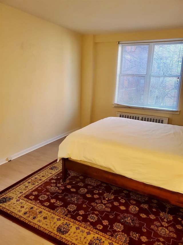 bedroom with baseboards, wood finished floors, and radiator