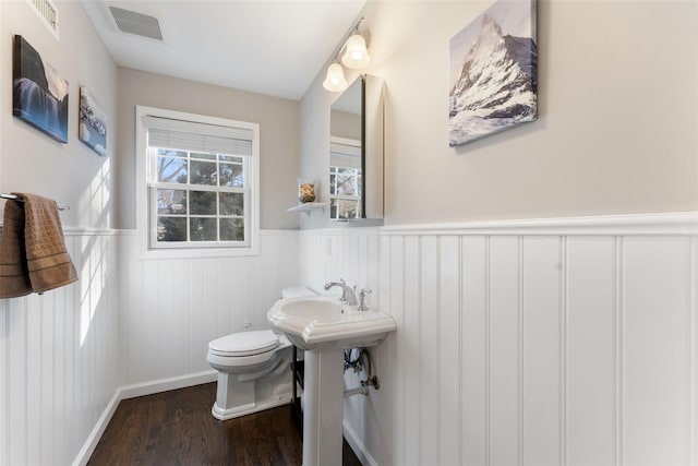 half bath featuring a wainscoted wall, toilet, wood finished floors, and visible vents