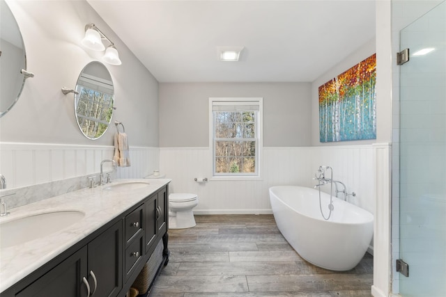 full bathroom featuring a wainscoted wall, a freestanding bath, a sink, and wood finished floors