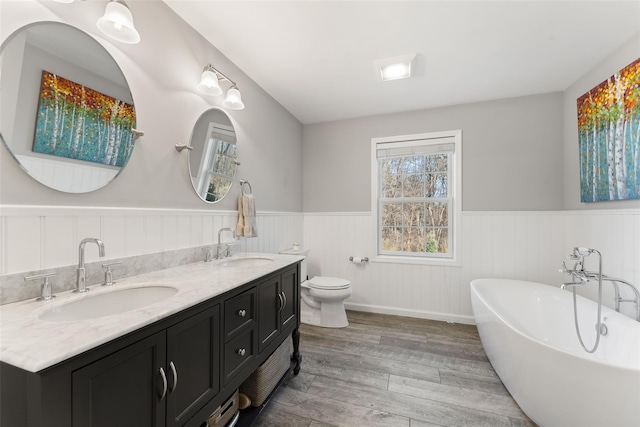 bathroom with a soaking tub, a wainscoted wall, a sink, and wood finished floors