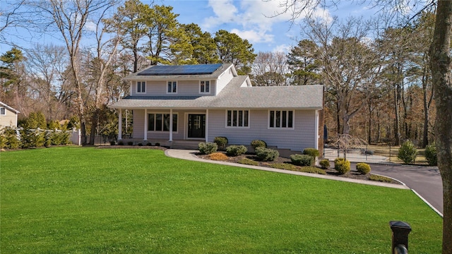 view of front facade with aphalt driveway, a porch, fence, roof mounted solar panels, and a front yard