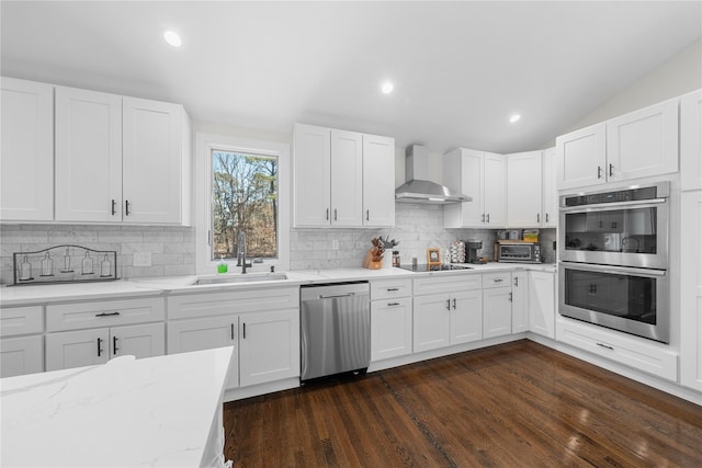 kitchen with stainless steel appliances, a sink, white cabinetry, backsplash, and wall chimney exhaust hood