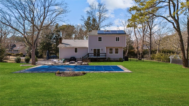 rear view of property featuring a lawn, solar panels, a covered pool, a wooden deck, and a patio area