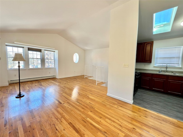 interior space with a sink, baseboards, vaulted ceiling, baseboard heating, and light wood finished floors