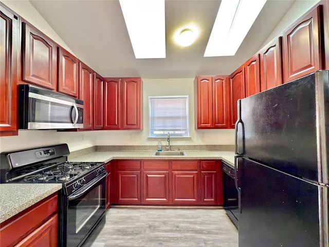 kitchen with a skylight, light wood-style flooring, dark brown cabinets, black appliances, and a sink