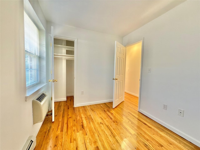 unfurnished bedroom featuring an AC wall unit, light wood finished floors, a closet, and baseboards