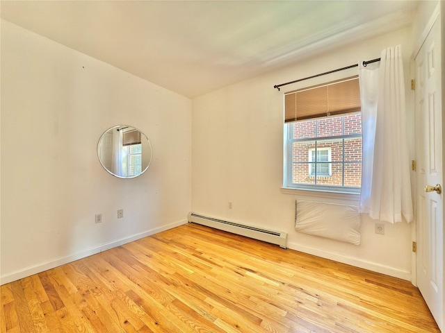 empty room featuring baseboard heating, wood finished floors, and baseboards