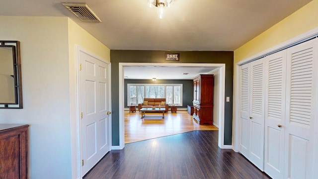 hall featuring visible vents, baseboards, and dark wood-style flooring