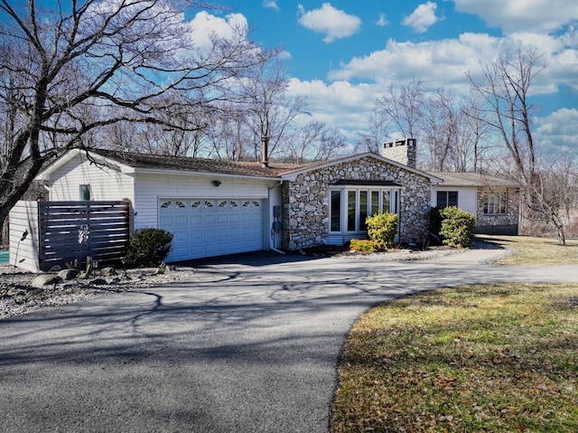 view of front of property with aphalt driveway, a garage, stone siding, and a chimney