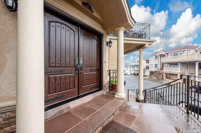 view of exterior entry with a balcony, a residential view, and stucco siding