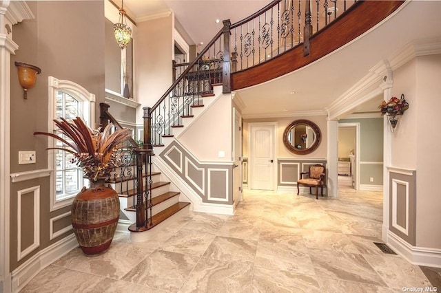 foyer entrance with stairs, ornamental molding, a towering ceiling, and a decorative wall