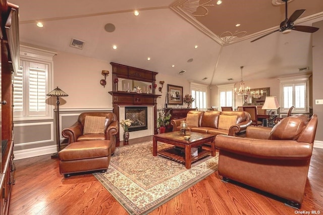 living area with ceiling fan with notable chandelier, a glass covered fireplace, visible vents, and wood finished floors