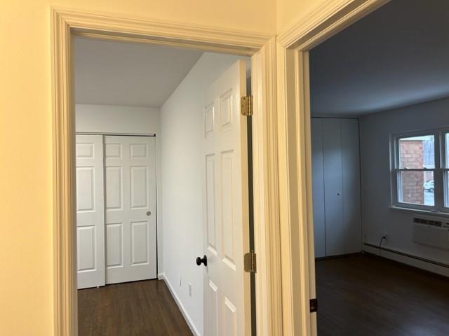 hall with dark wood-type flooring, a baseboard radiator, and baseboards