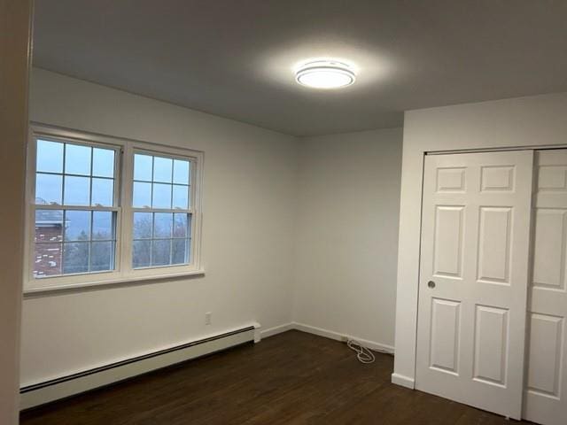 unfurnished bedroom with dark wood-style floors, baseboards, baseboard heating, and a closet