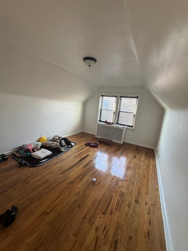 additional living space featuring vaulted ceiling, radiator heating unit, wood-type flooring, and baseboards