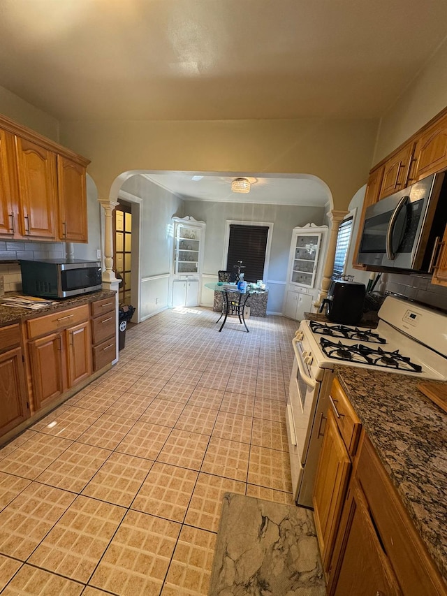 kitchen featuring ornate columns, white range with gas cooktop, arched walkways, and stainless steel microwave