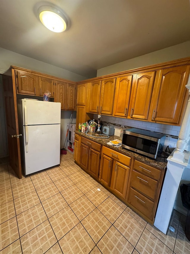 kitchen featuring tasteful backsplash, brown cabinetry, stainless steel microwave, freestanding refrigerator, and a sink