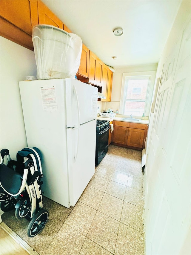 kitchen with light countertops, brown cabinetry, freestanding refrigerator, black gas stove, and a sink